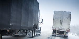 Two semi-trucks driving in the snow.